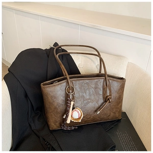 Detail of dark brown tote bag with vintage texture and baseball bat charm on a sofa