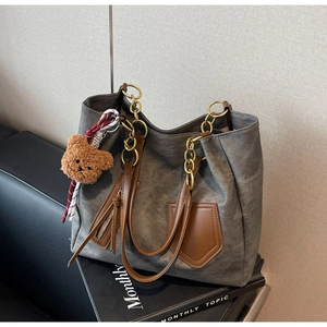 Detail of grey textured tote bag with brown leather trim and golden chain strap