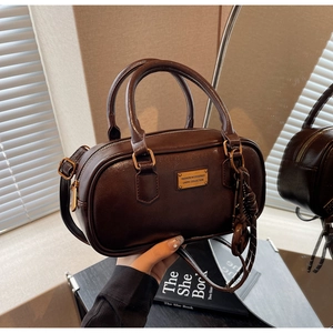 Detail der dunkelbraunen Boston-Tasche mit glänzendem Leder und goldenem Logo-Schild