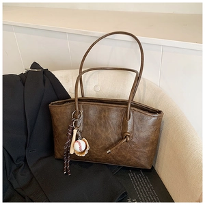 Detail of vintage brown tote bag with smooth leather texture and baseball glove pendant