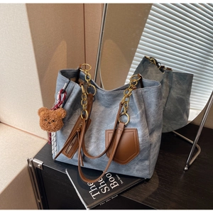Detail view of washed blue canvas tote with brown leather trim and golden chain strap