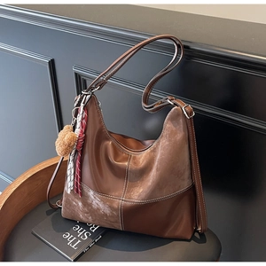 Détail du sac Hobo marron avec surpiqûres blanches et pompon en peluche sur un siège
