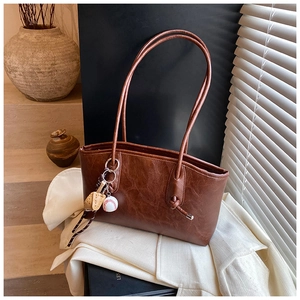 Detailed view of brown retro shoulder bag with litchi texture and baseball charm
