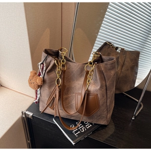 Macro detail of dark brown leather tote with gold chain strap and bear charm
