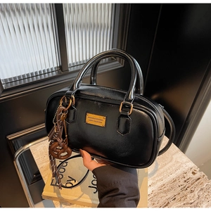 Detail der schwarzen glänzenden Ledertasche mit goldener Hardware und braunem Knotanhänger