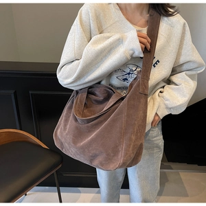 Close-up of a large coffee brown suede tote bag worn by a model in a modern room
