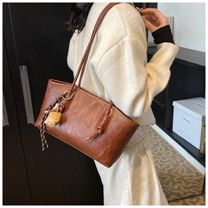 Brown leather tote bag with long straps and yellow animal charm in casual setting