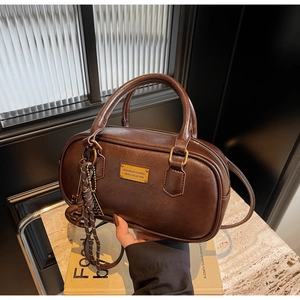 Detail der braunen Boston-Tasche mit polierter Ledertextur und Metallnamensschild