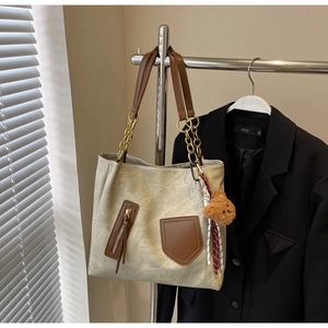 Detail view of large tote bag with brown leather accents and a teddy bear charm