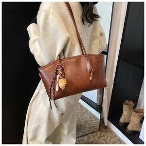 Detail of red-brown PU leather tote bag with stylish charms and checkered ribbon detail