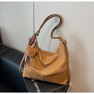 Détail d'un sac cabas marron en similicuir avec coutures blanches et charm ours peluche