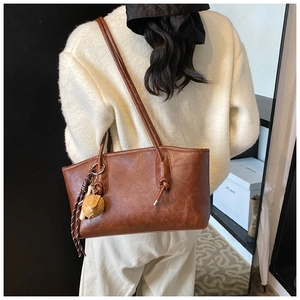 Brown vintage faux leather tote bag with ball pendant shown in a lifestyle shoulder view