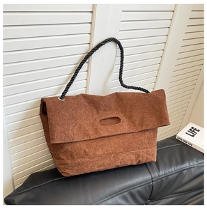 Close-up of vintage brown corduroy tote bag with black braided rope handles on leather bench