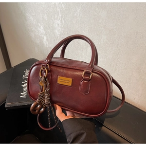 Nahaufnahme der tiefroten Boston-Tasche mit Glanzfinish und goldenen Dekorguard-Anhänger
