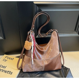 Détail d'un sac Hobo marron avec coutures contrastées et un joli pendentif ours