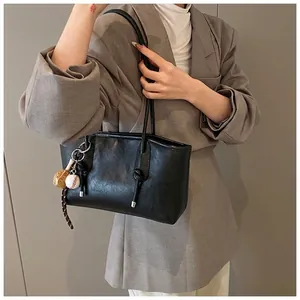 Detail of black faux leather tote bag with unique baseball pendant and button accents