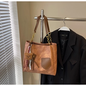 Detail of vintage brown tote bag featuring chain straps and a plush bear pendant charm