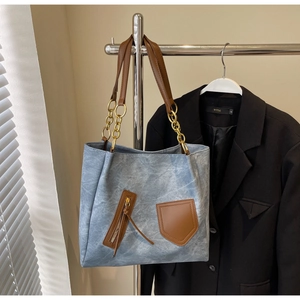 Close-up of a blue denim tote bag featuring brown leather straps and gold chain accents