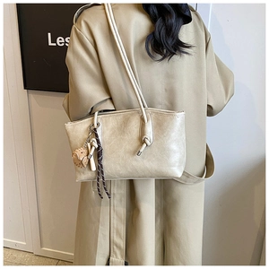 Detail of beige tote bag with knotted strap and heart charm on a trench coat model
