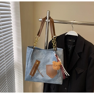 Close-up of contrast color tote bag with plush bear charm and metallic chain detail