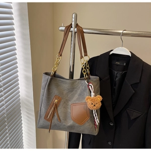 Detail of grey tote bag with brown leather handles and cute plush bear charm accessory