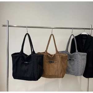 Close-up of plush tote bags in black, brown, and grey hanging on a metal rack