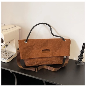 Detail of a brown corduroy tote bag featuring a black twisted handle and adjustable strap