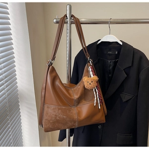 Détail d'un sac cabas demi-lune marron avec surpiqûres blanches et charme d'ours mignon
