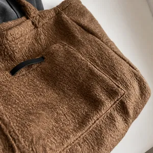 Detail shot of brown plush tote bag showing soft sherpa texture and black leather trim
