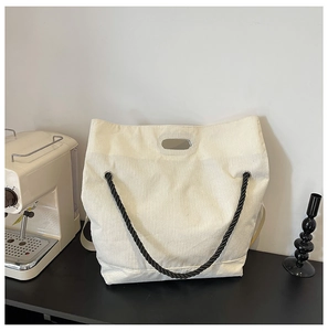 Close-up of beige corduroy tote bag featuring vertical texture and black woven rope handle