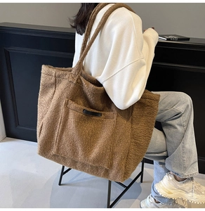 Detail of large brown plush tote bag with front pocket carried by a model in casual wear