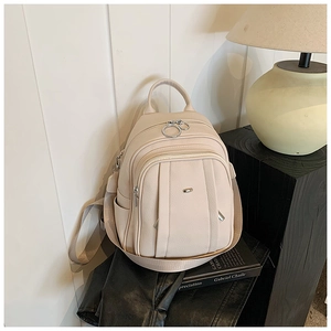 Detail eines cremeweißen Rucksacks mit Lychee-Struktur, mehreren Reißverschlüssen und Ringen