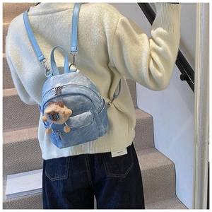 Lichtblauwe mini-rugzak met denimtextuur en bruine pluchen beer hanger op een model