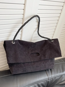 Minimalist black corduroy tote bag with woven handles shown on a vintage leather sofa