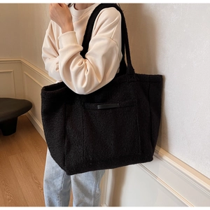 Detail of a black oversized faux shearling tote bag with a front pocket on a model
