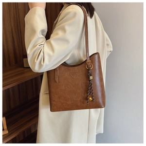 Détail du sac cabas en cuir mat marron avec pompon tressé et décoration de clochette dorée