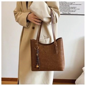 Détail d'un sac cabas en cuir marron avec pendentif clochette dorée et bandoulière