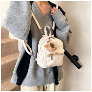 Detailweergave van een witte mini-rugzak met zachte textuur en schattig pluche hangertje.