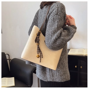 Détail du sac cabas crème avec lanières en cuir marron et pendentif cloche décoratif