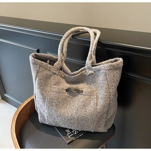 Detail of grey plush tote bag with front pocket and faux leather buckle on a dark chair