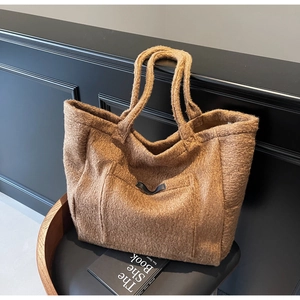 Detail view of brown plush tote bag with lamb wool texture and front pocket on chair