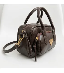 Détail du sac Boston en cuir marron foncé avec texture litchi et finitions dorées