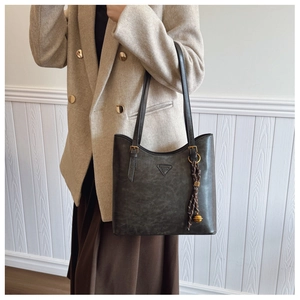 Détail d'un sac cabas vintage gris avec pompon porté à l'épaule sur un blazer