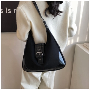 Detail of black semi-circle shoulder bag with large metal buckle worn on model