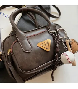 Détail du sac Boston en cuir marron foncé avec logo en métal et breloques de baseball
