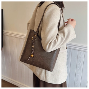 Détail du sac cabas marron foncé avec breloque tressée sur une tenue de tailleur blanc