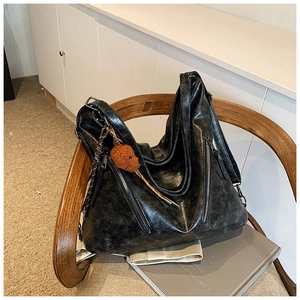 Detail of a black oil wax leather tote bag with side zippers and a plush dog charm on a chair