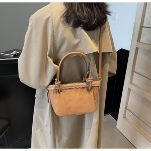 Detail view of brown suede bucket bag with beige faux fur trim and leather top handle