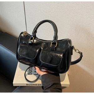 Detail of black glossy Boston bag showing polished surface and front pockets with golden hardware