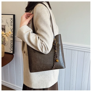 Détail du sac cabas marron foncé avec texture vintage et breloque dorée sur l'épaule